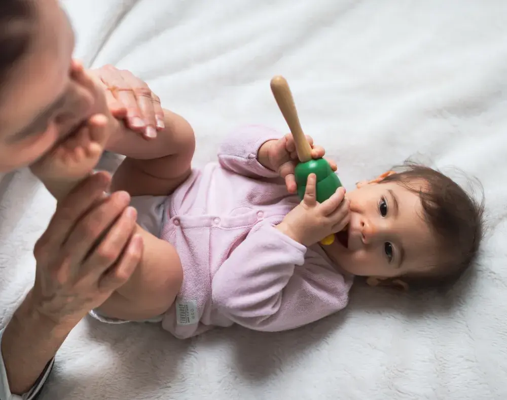baby lies on a mat with a rattle while parent or caregiver kisses feet